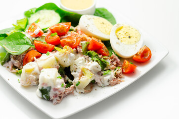 Healthy salad, potato salad with hard boiled egg, shredded ham, cucumber, tomatoes, lettuce and spinach with a honey and mustard dressing pot