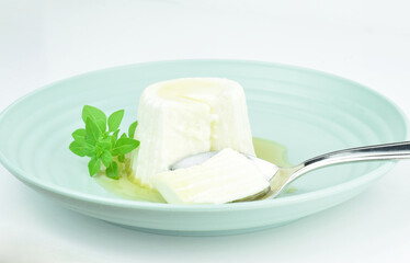 Close up, fresh cheese with honey served on a plate, with a sprig of basil. Light background and copy space.