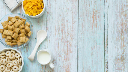 Different types of cereal in plates and a jug of milk on a wooden background