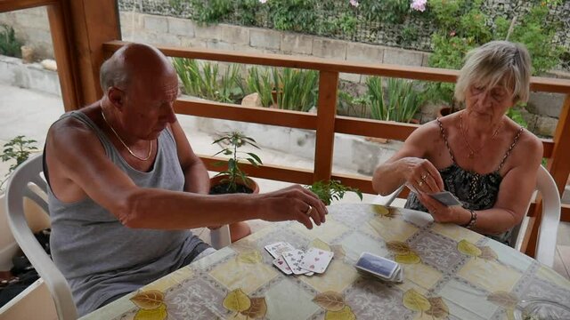 elderly retired couple, husband and wife, play rummy in the summer, under a gazebo in the garden.