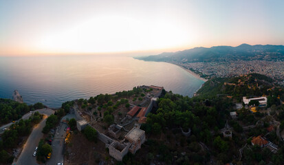 Large panorama. Wide aerial view of Alanya bay, Turkey, Summer sunset evening, night time. Travel and vacation. Kalesi Castle. Ships and boats at sea. City lights. Streets and houses.