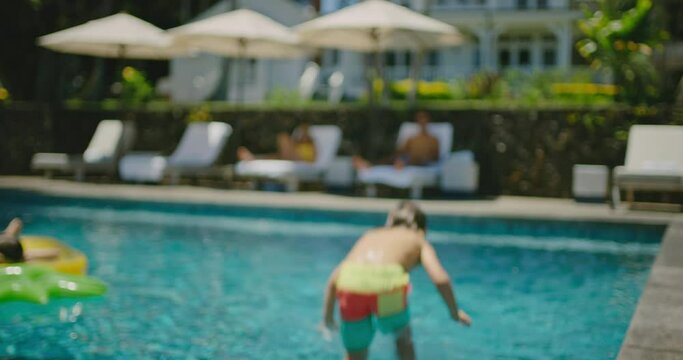 Happy young boy running and jumping into the pool, family lifestyle, summer vacation concept