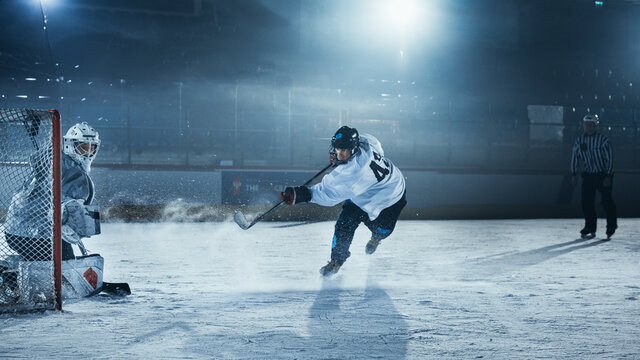 Ice Hockey Rink Arena: Goalie is Ready to Defend Score against Forward Player who Shoots Puck with Stick. Forwarder against Goaltender One on One. Tension Moment in Sport Full of Emotions.