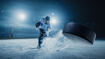 Ice Hockey Rink Arena: Professional Player Shooting the Puck with Hockey Stick. Focus on 3D Flying Puck with Blur Motion Effect. Dramatic Wide Shot, Cinematic Lighting. - obrazy, fototapety, plakaty