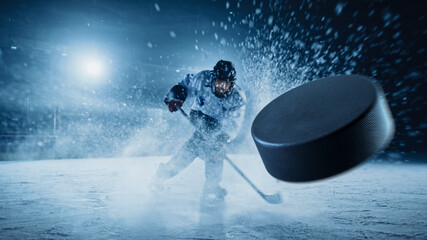 Fototapeta Ice Hockey Rink Arena: Professional Player Shooting the Puck with Hockey Stick. Focus on 3D Flying Puck with Blur Motion Effect. Dramatic Wide Shot, Cinematic Lighting. obraz