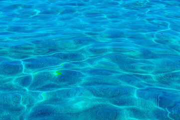 Fototapeta na wymiar Marine background. Transparent turquoise-blue sea water against the background of white sand below, top view. Sun glare on the surface. High quality photo