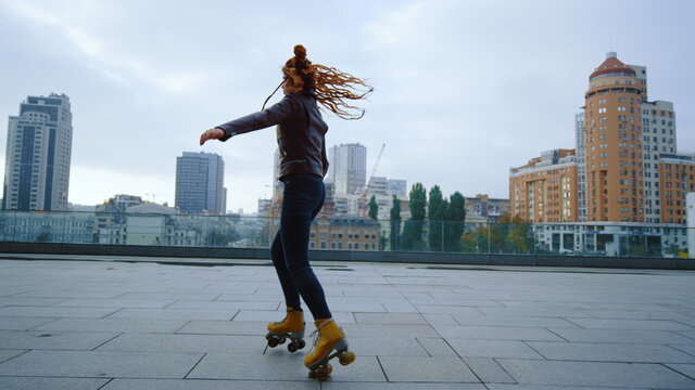Sporty ginger woman performing elements of rollerblading on urban background.