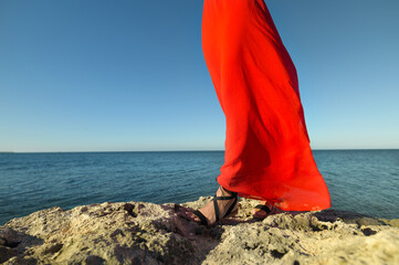 Lovely romantic caucasian young woman in red dress and straw hat against the background of the sea...