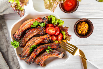  Baked pork ribs with vegetables, mustard and ketchup on white wooden background top view