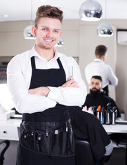 Smiling young man hairdresser demonstrating his workplace and tools at salon