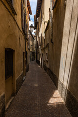Fototapeta premium Very narrow alley in Bellano, lake Como, Lombardy, Italy. Narrow alley between the residential buildings in the small town of Bellano by the Como lake, Lombardy, Italy. Just a little sun comes down