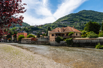 Fototapeta na wymiar Stock photo of river Pioverna in the city of Bellano, in Lake Como, Lombardy, Italy. Picture taken upstream. There are houses and hills behind the river. It is a beautiful sunny summer day