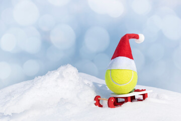Christmas creative composition with yellow tennis ball in red Santa hat sleigh ride on white snow...