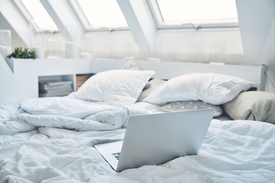 Image of laptop laying on bed with pillows and nanket around