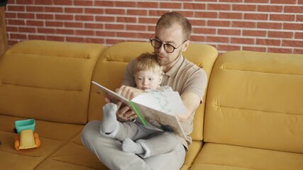 Father reading book aloud to cute son at home