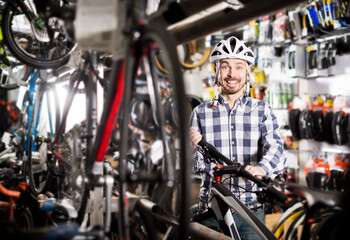 Glad man in helmet chooses convenient bike to ride in sports store