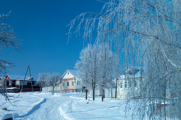 A street in the village in winter. Rural landscape against the blue sky