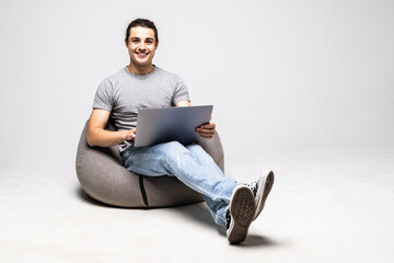 Handsome young man isolated on white background. Man smiling, using laptop and sitting on big cushioned frameless chair