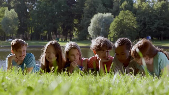 Joyful multiracial preteen friends lying on park grass together