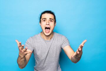 Emotional overjoyed young unshaven man keeping mouth wide opened and holding hands at his face,...