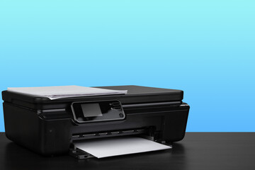 Compact laser printer on black desk against blue background