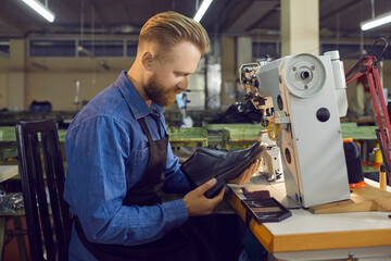 Skilled male employee of a shoe factory checks the quality of men's leather shoes at his workplace....