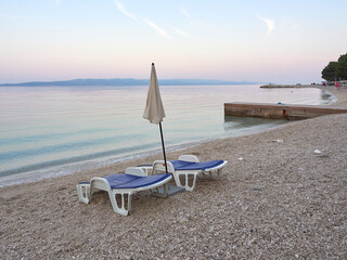 Empty sun loungers and umbrella on Podluka beach in Baska Voda. A seaside resort waiting for tourists. A beautiful quiet morning on the Adriatic in a Croatian city