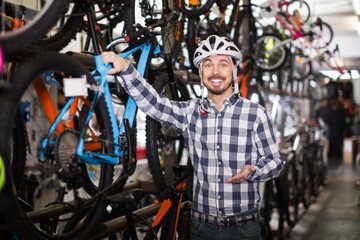 Fototapeta na wymiar cheerful man in helmet chooses for himself sports bike in bicycle shop from a range