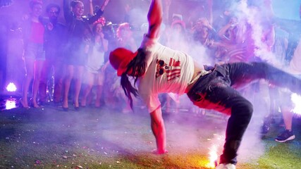 Break dancer dancing with firework sticks on night colorful party with many young people. Boy performed dances with fireworks in the night during party . Firework in hand . Red Camera in Slow motion. 