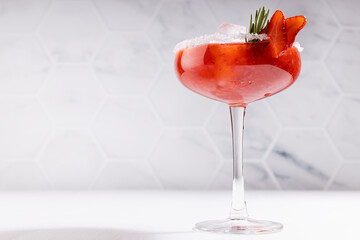 Bright fresh strawberry margarita cocktail with ice, green rosemary twig, sugar rim, fruit slices...