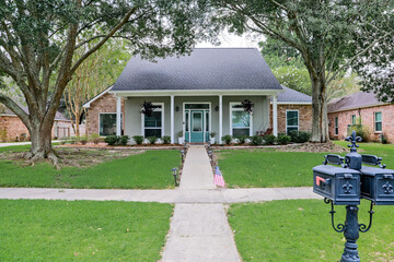 A front view of an Acadian renovated home with columns, sidewalks and a colorful front door...