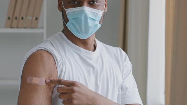 Moving footage african sick man patient wears face protective mask points finger at medical patch on shoulder vaccination mark injection puts thumbs up approves immunization contented with medication