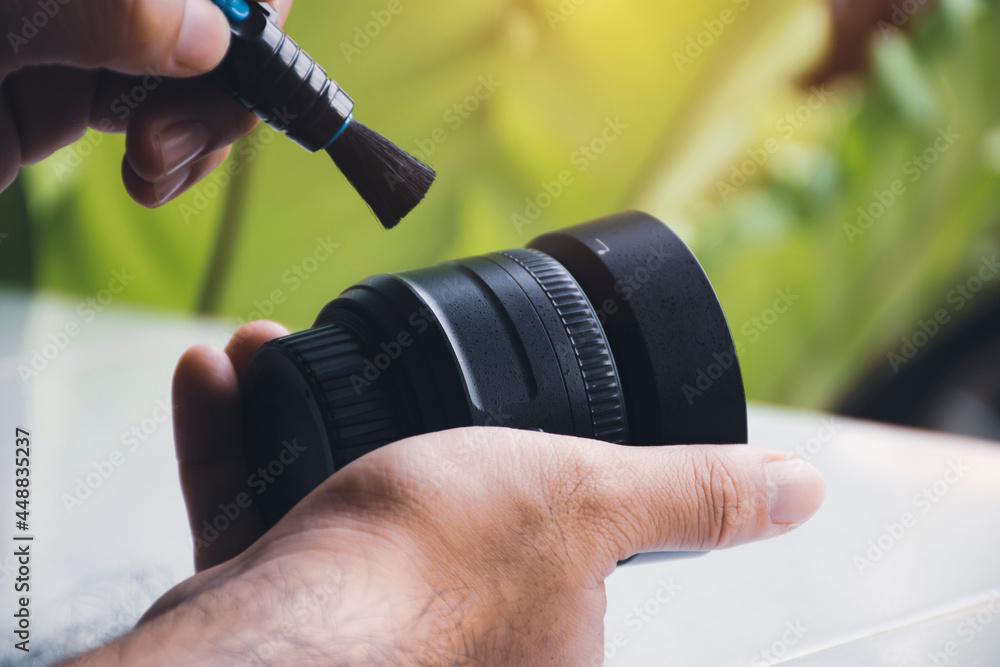 Wall mural human hand cleaning dust on camera lens with pen brush cleaner