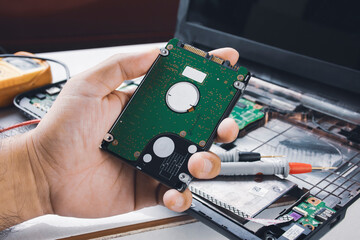 Hard disk drives 2.5 inch (HDD) holding on the mechanic hand with computer laptop and multimeter probe background