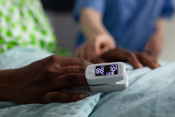 Close up of oximeter on african american girl hand laying in hospital ward bed. Device showing low oxygen saturation and pressure measurement used on young patient with disease. Medical equipment