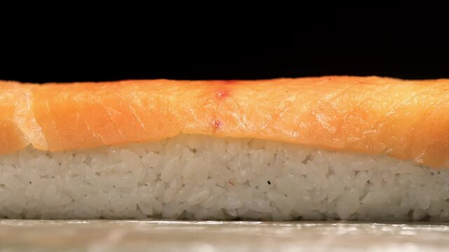Hand of sushiman lays out salmon fillet on roll, macro, side view. Closeup preparation of rolls. Japanese cuisine concept