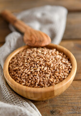 Fototapeta na wymiar Wholegrain uncooked raw spelt farro in bowl on the wooden background, food cereal background, close up