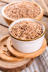 Wholegrain uncooked raw spelt farro in bowl on the wooden background