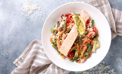 Seafood dish. Red fish with rice and vegetables. Salmon with lemon, beans, carrots, peas and cauliflower in a white plate on a gray table. Background image, copy space, top view