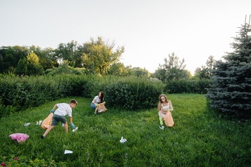 A group of girls with children at sunset are engaged in garbage collection in the park. Environmental care, recycling.