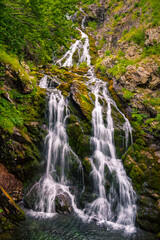 Gran cascada de un rio de montaña cae entre rocas cubiertas de musgo verde.