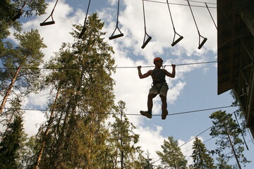 boy wearing a safety harness and a helmet walking in a rope park