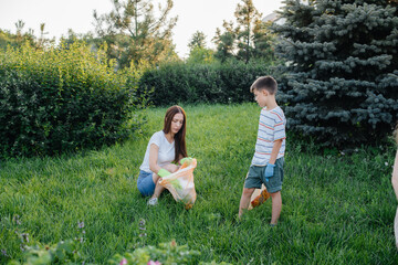 Obraz premium A group of girls with children at sunset are engaged in garbage collection in the park. Environmental care, recycling.