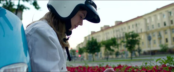 Blonde female wearing motorcycle white helmet. Girl sits on a motorbike and uses a mobile phone. Closeup of delivery biker - Powered by Adobe