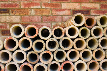 Terracotta clay brick pipes stacked against red brick wall with copy space