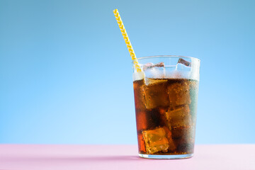 A glass of cola with ice on blue and pink background