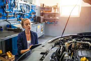 Female mechanic working on car tyre service. Portrait Of Female Auto Mechanic Working Underneath Car. Portrait of smiling young female mechanic inspecting a CV joing on a car in auto repair shop