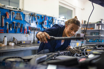 Mechanic working under the hood at the repair garage. Portrait of a happy mechanic woman working on...