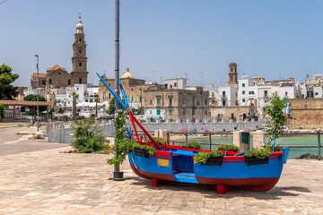 tradycyjna niebiesko czerwona łódź rybacka na tle panoramy starówki w Monopoli, Puglia, Włochy - obrazy, fototapety, plakaty