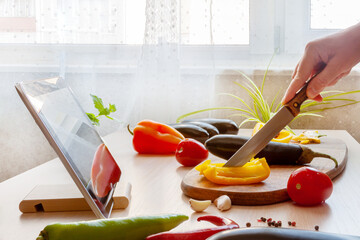 Woman slicing pepper watching online culinary class her tablet, cooking vegan food with fresh...